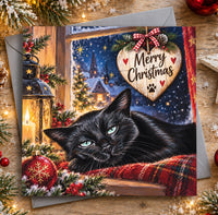Black cat Christmas card featuring a beautiful black cat with green eyes resting beside a snowy window and wooden Merry Christmas heart decoration.