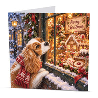 Square Cavalier King Charles Spaniel Christmas card featuring a festive dog in a snowy street beside a decorated Christmas shop window